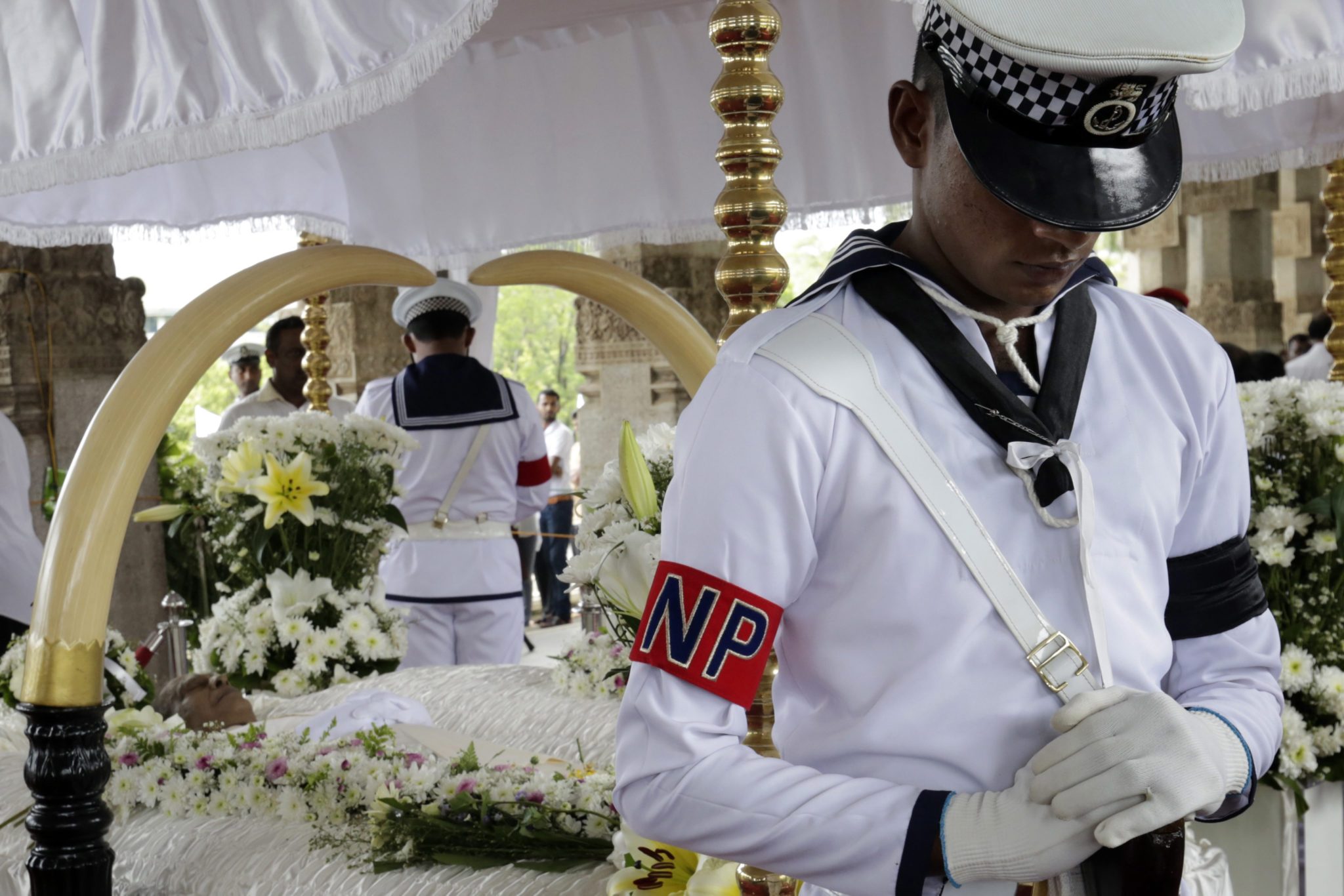 Policyjny marynarz pilnuje zachowania szacunku przy szczątkach Sri Lanckiego muzyka Pandita Amaradevy. Sri Lanka, 5 listopada 2016