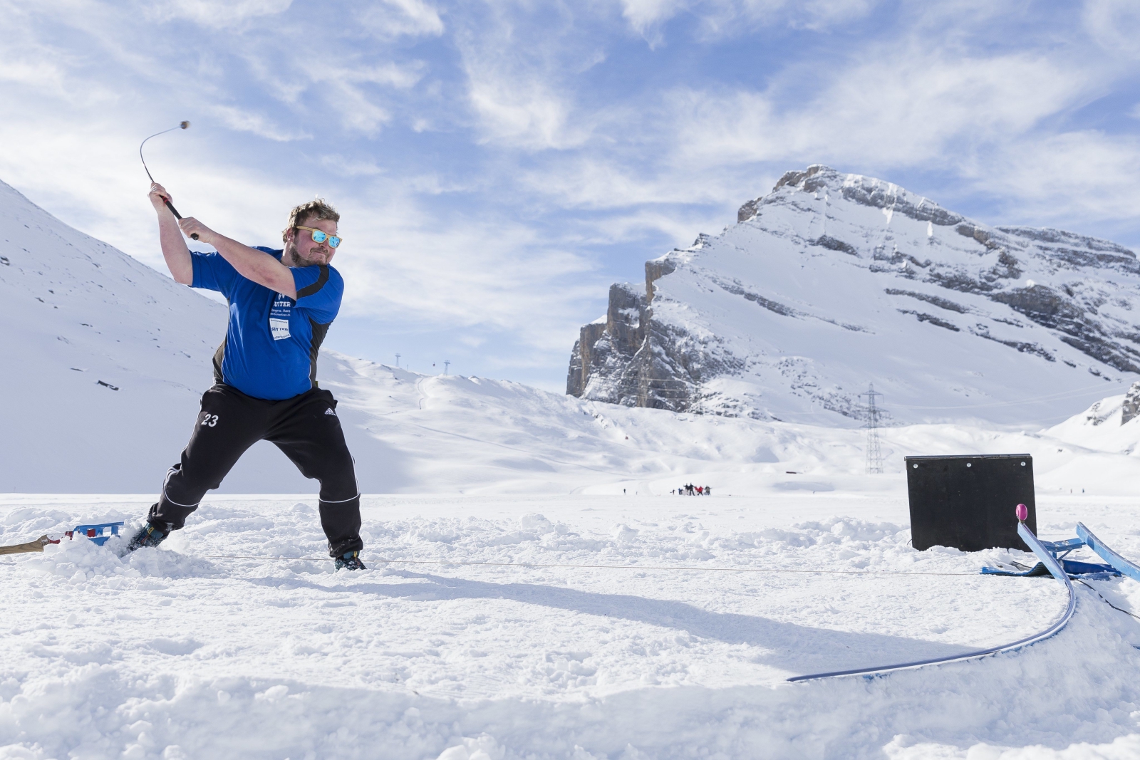 Mężczyzna gra w grę Hornussen na śniegu pokrywającym zamarznięte jezioro Dauben w Alpach Szwajcarskich.