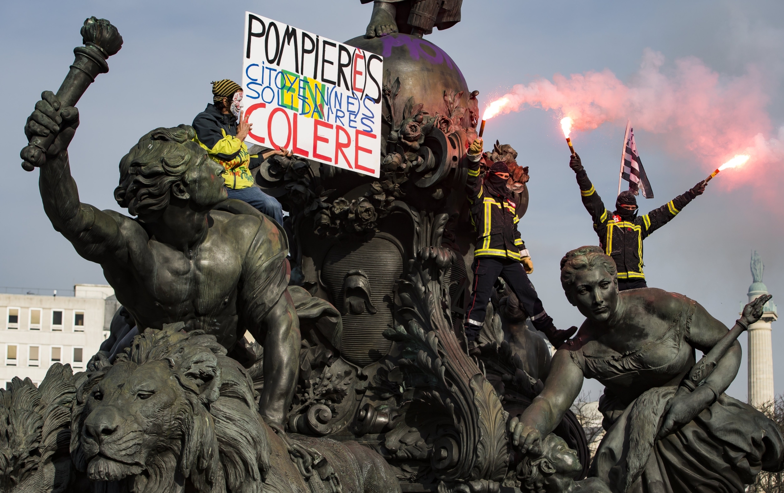 Francuscy strażacy wymachują racami na szczycie pomnika w trakcie protestu, Paryż, Francja.