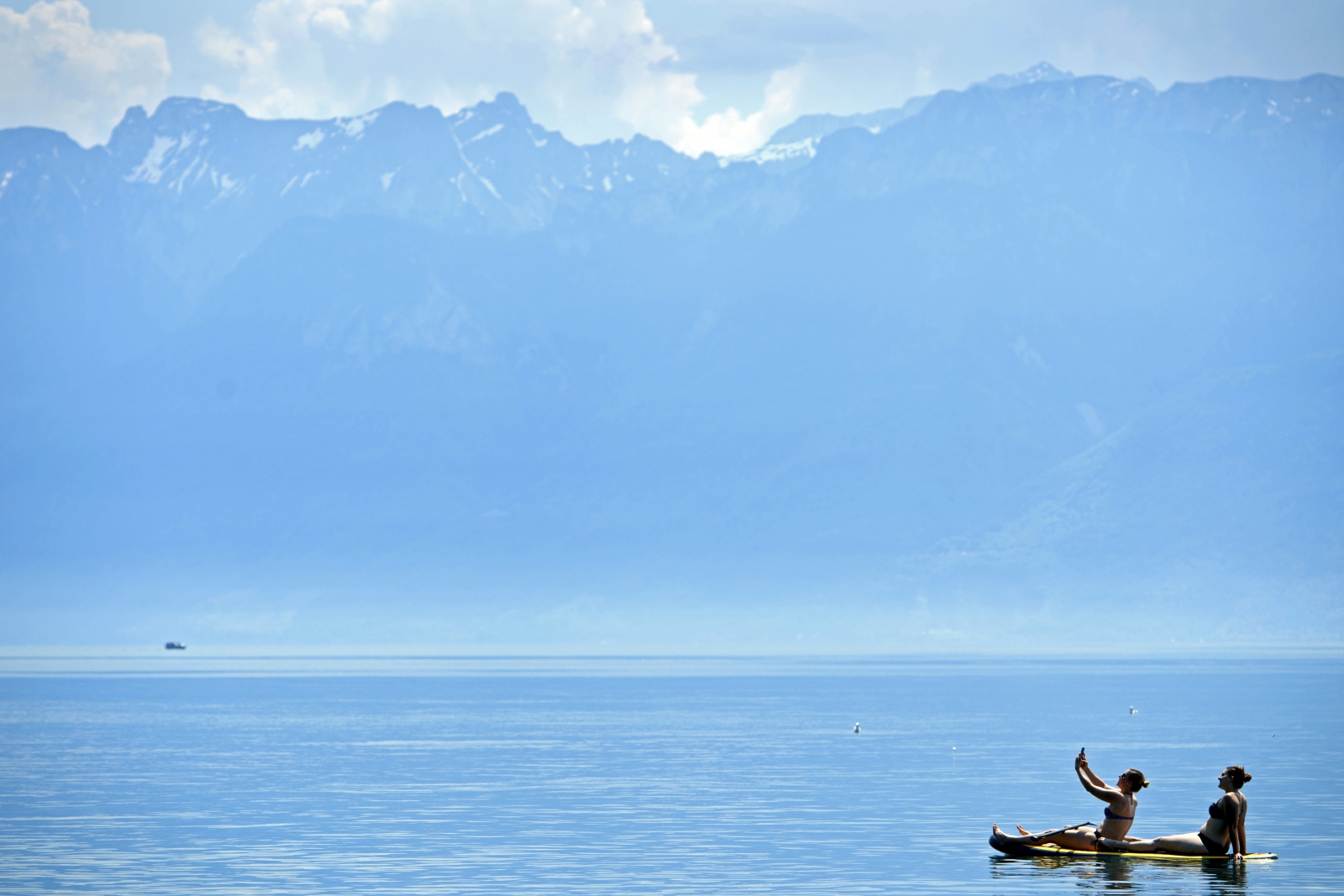 Ludzie korzystają z dobrej pogody na jeziorze Genewskim. W tle francuskie i szwajcarskie Alpy.
