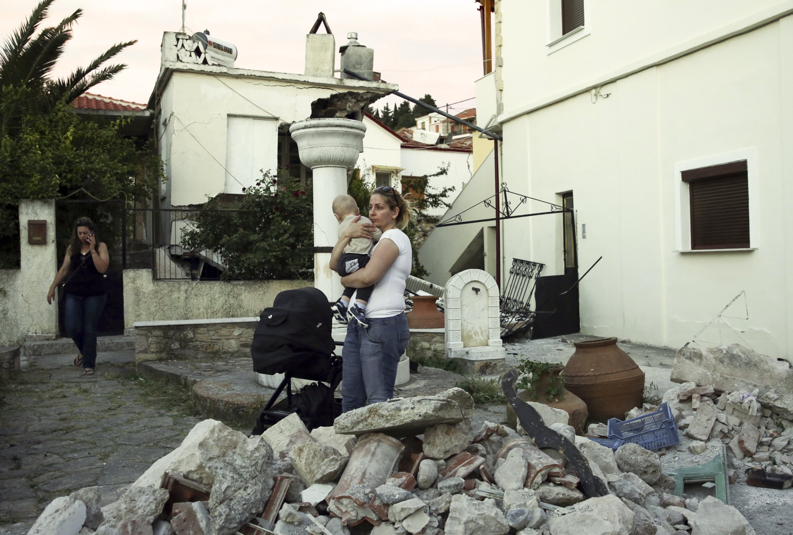 Kobieta trzymająca dziecko stoi w ruinach domu po trzęsieniu ziemi, które nawiedziło wyspę Lesbos.
