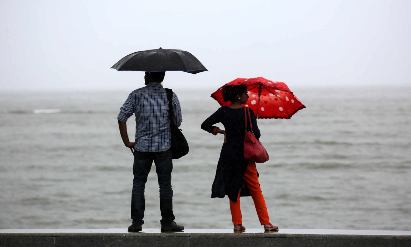 Ludzie stojący na promenadzie chronią się przed monsunowym deszczem pod parasolami, Indie.