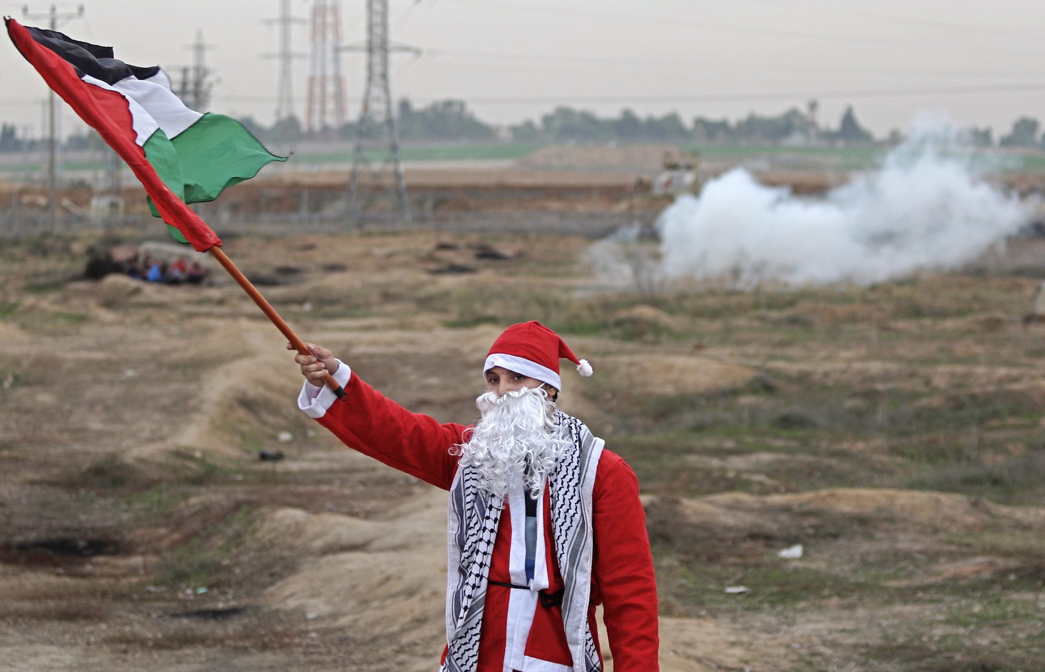Palestyński protestant przebrany za Świętego Mikołaja macha flagą palestyńską podczas starć po protestach przeciwko decyzji prezydenta USA Trumpa o uznaniu Jerozolimy za stolicę Izraela, w pobliżu granicy z Izraelem, na wschód od Strefy Gazy, fot: Mohammed Saber, fot: PAP/EPA 