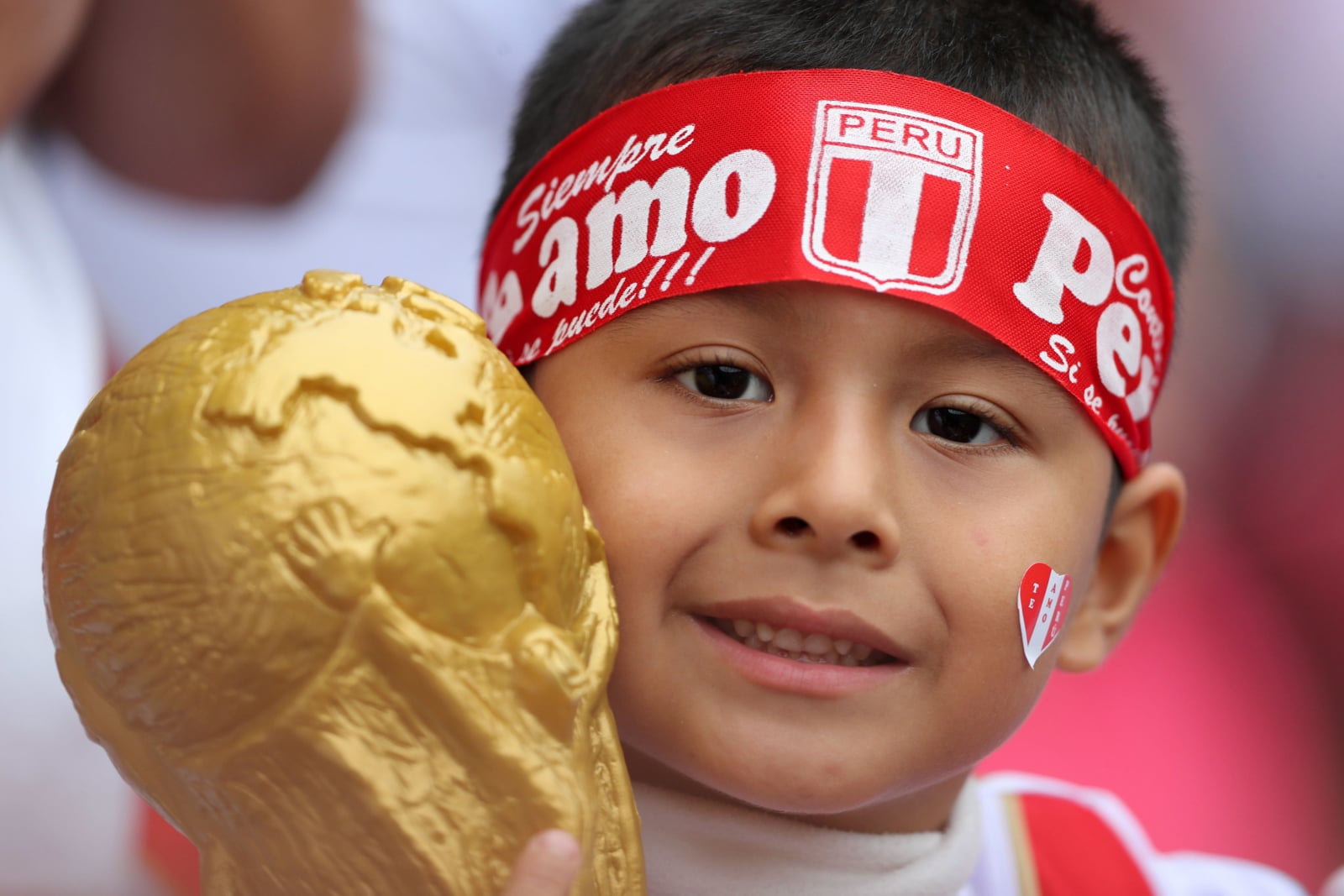 Mały peruwaińczyk trzyma replikę trofeum Mistrzostw Świata w piłce nożnej.