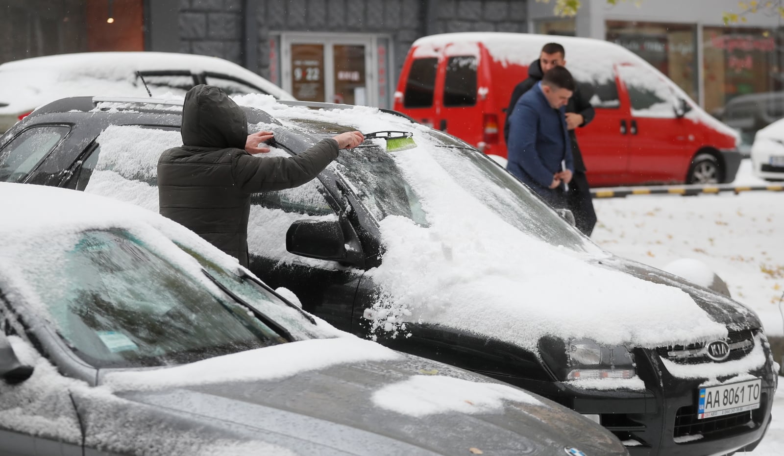 Mieszkaniec Kijowa czyści swój samochód ze śniegu na ulicy, Ukraina. 