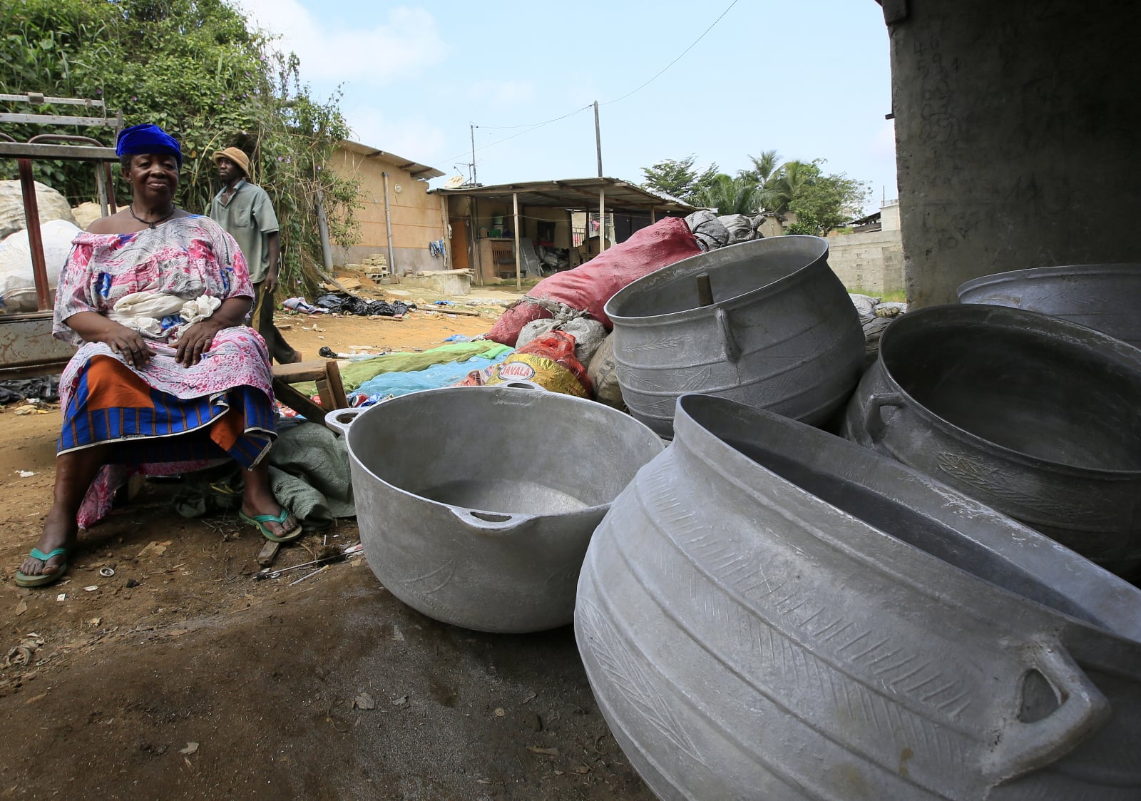 Kobieta siedząca przy garnkach do gotowania z odpadów metalowych w magazynie recyklingu w Abobo, Abidżan.