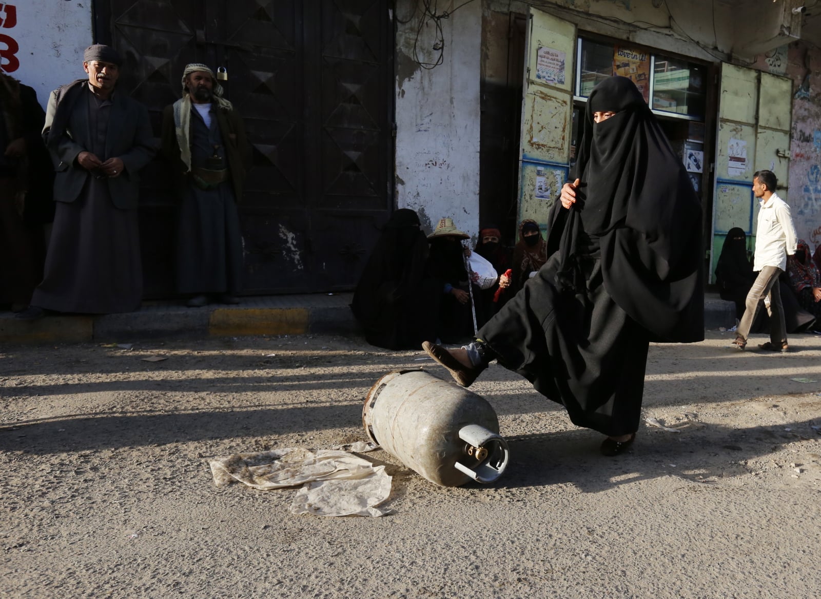 Jemeńska kobieta wyrzuca pustą butlę z gazem do gotowania, szukając zapasów gazu na ulicy. W Jemenie trwa kryzys humanitarny