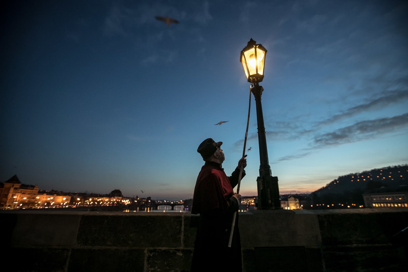 Latarnik Jan Tater zapala zabytkową lampę gazową na Moście Karola w Pradze, Czechy.