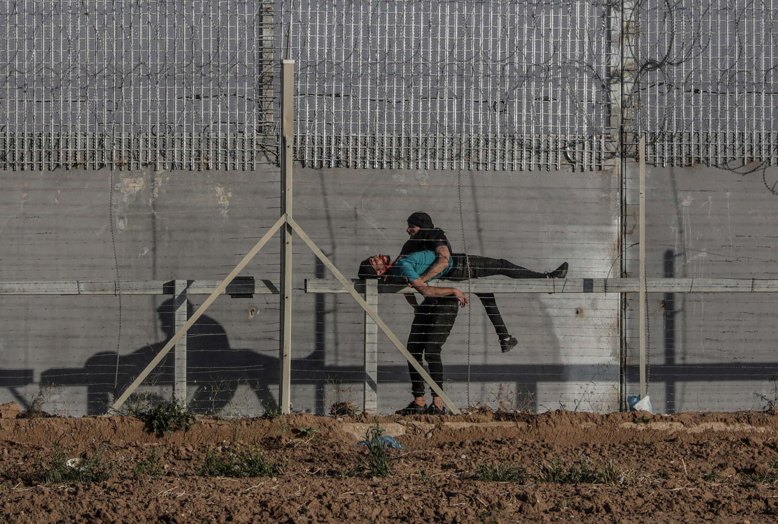 Palestyńczyk próbuje pomóc swojemu rannemu koledze. Fot. EPA/MOHAMMED SABER