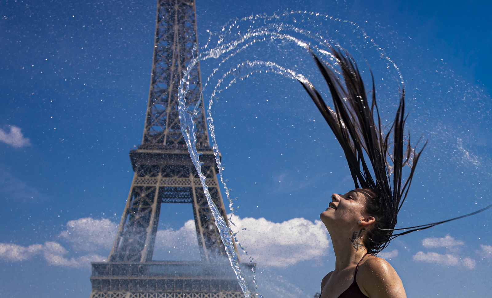 Dziewczyna ochładza się w fontannie naprzeciwko wieży Eiffla. Fot. PAP/EPA/IAN LANGSDON