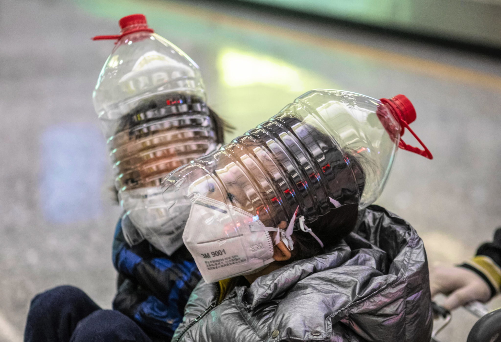 Chłopcy w maskach ochronnych, rękawiczkach i butelkach na głowie w terminalu przylotów lotniska w Kantonie, w prowincji Guangdong, Chiny, fot. EPA / ALEX PLAVEVSKI