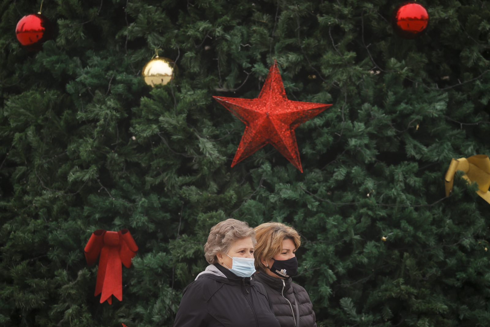 Piesi w ochronnych maskach na twarzy przechodzą obok udekorowanej choinki na głównym placu pośród trwającej pandemii koronawirusa COVID-19 w Prisztinie, Kosowo. Fot. EPA/VALDRIN XHEMAJ 